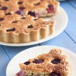 slice of cherry and coconut bakewell tart on plate in front with the whole tart behind