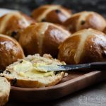 sourdough hot cross buns on a wooden platter with one being buttered